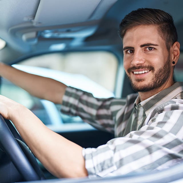 young caucasian man touching rearview sitting on car at street